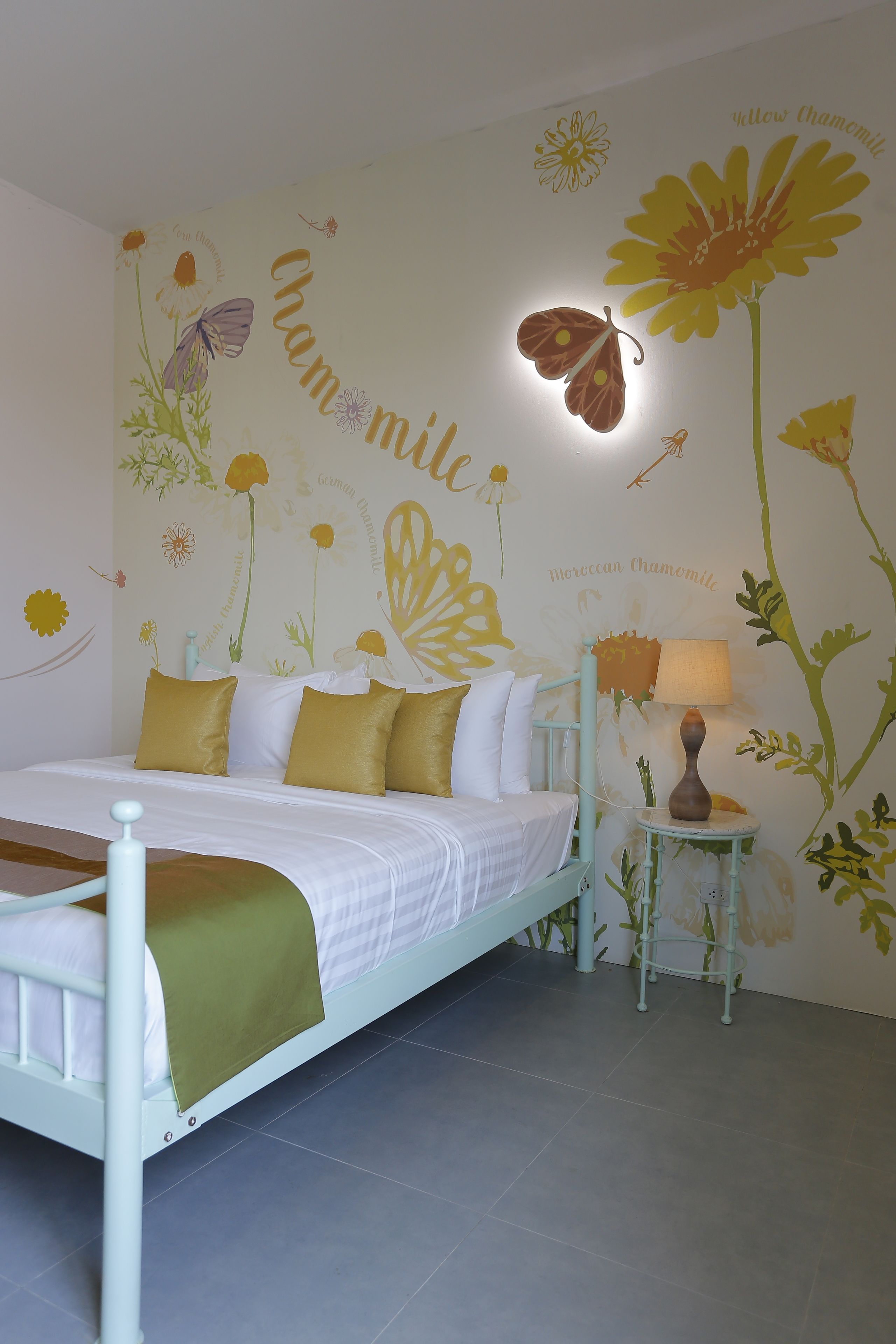 Un dormitorio con cama, almohadas, una mesita de noche y un mural en la pared.