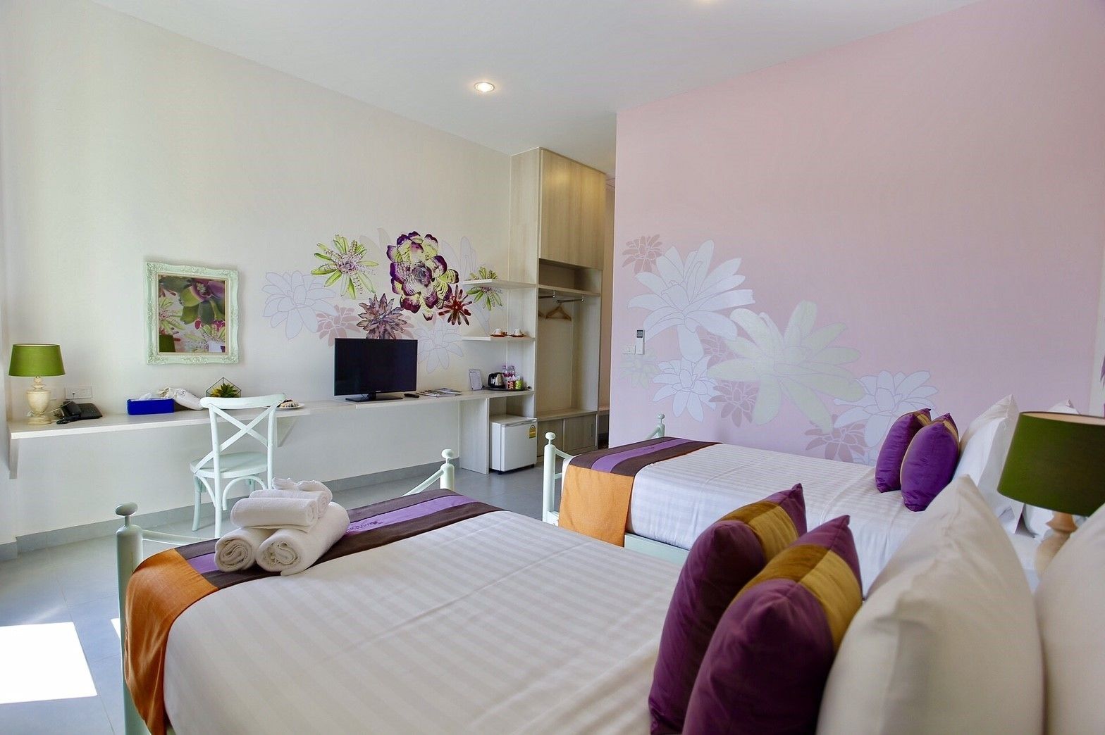 A hotel room with two beds, a desk with a computer, a chair, and a TV.