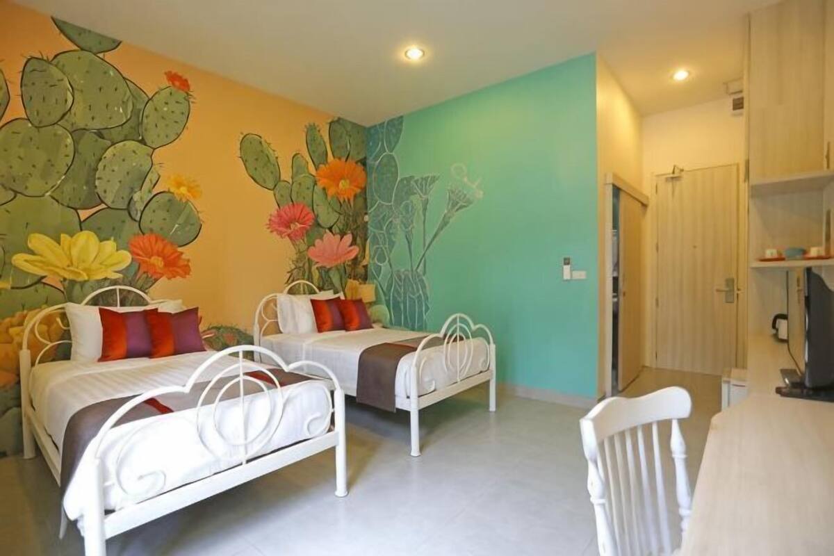 Un dormitorio con dos camas, un mural de cactus y una puerta que da a un baño.