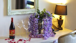 A table with a wine bottle, two glasses, and purple flowers.
