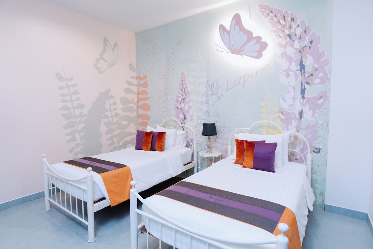 Habitación de hotel con dos camas, una mesita de noche y un muro decorado con motivos de mariposas y plantas.