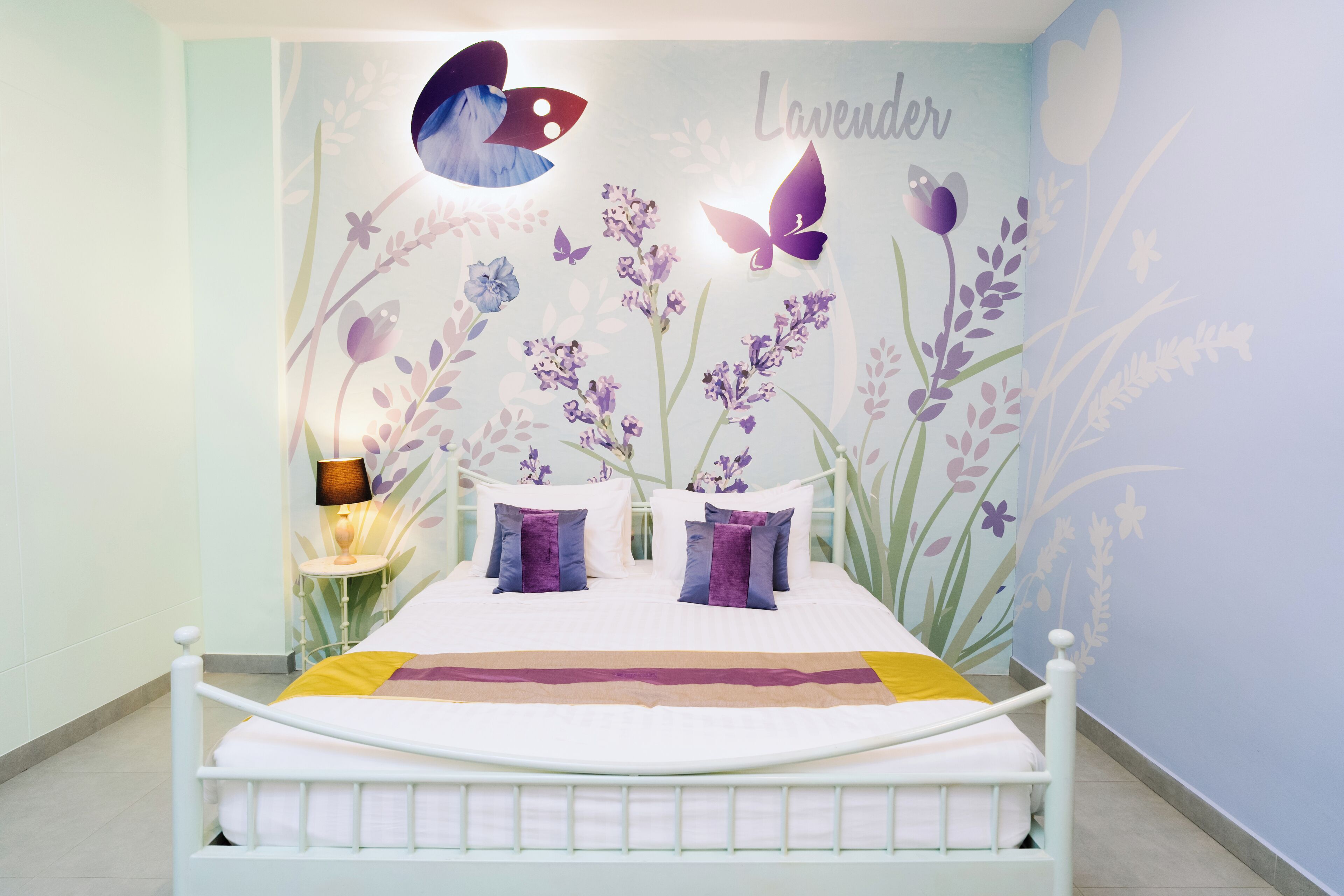 Un dormitorio con un mural floral, una cama con ropa de cama blanca y una lámpara de noche.