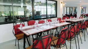 A conference room with long tables and red chairs, large windows, and indoor plants.