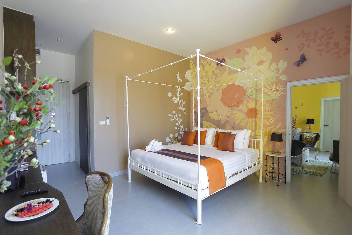 Una cama con dosel de estructura blanca, un mural floral en la pared y una pequeña mesa con una lámpara.