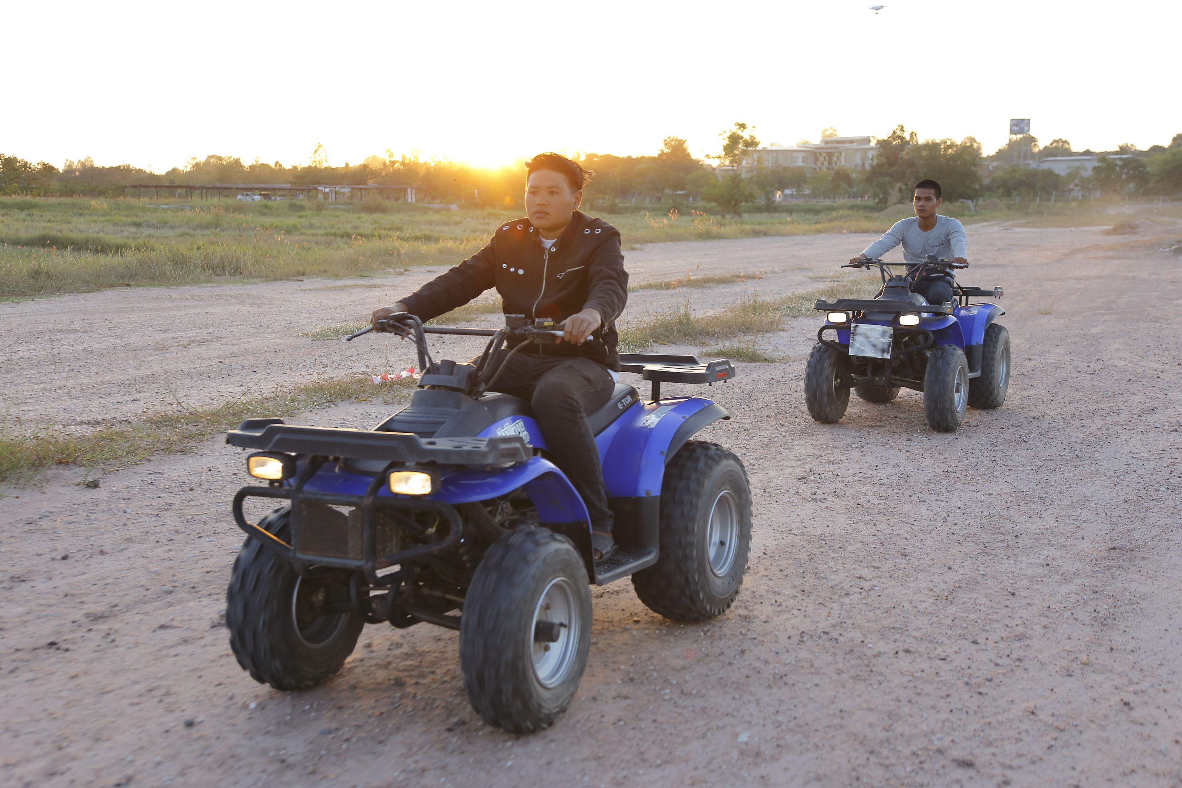Two people riding ATVs on a dirt road with a sunset in the background.