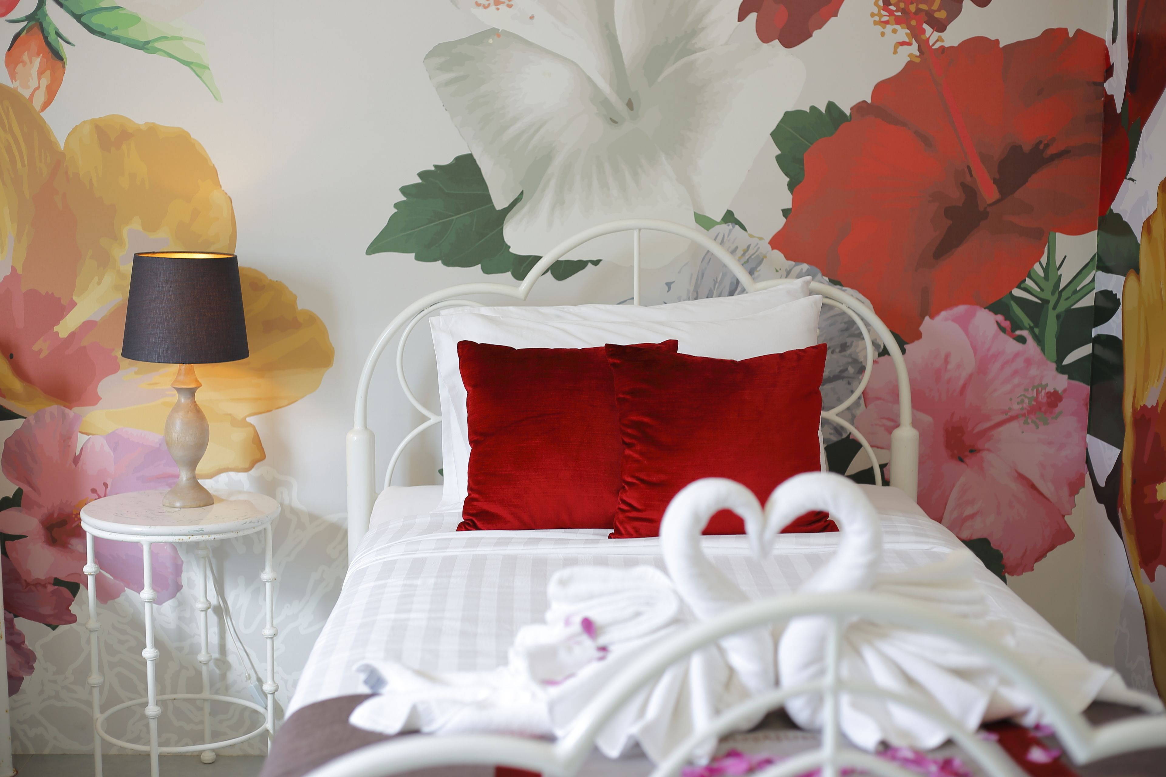 A neatly made bed with a white headboard, red pillows, and a white towel.