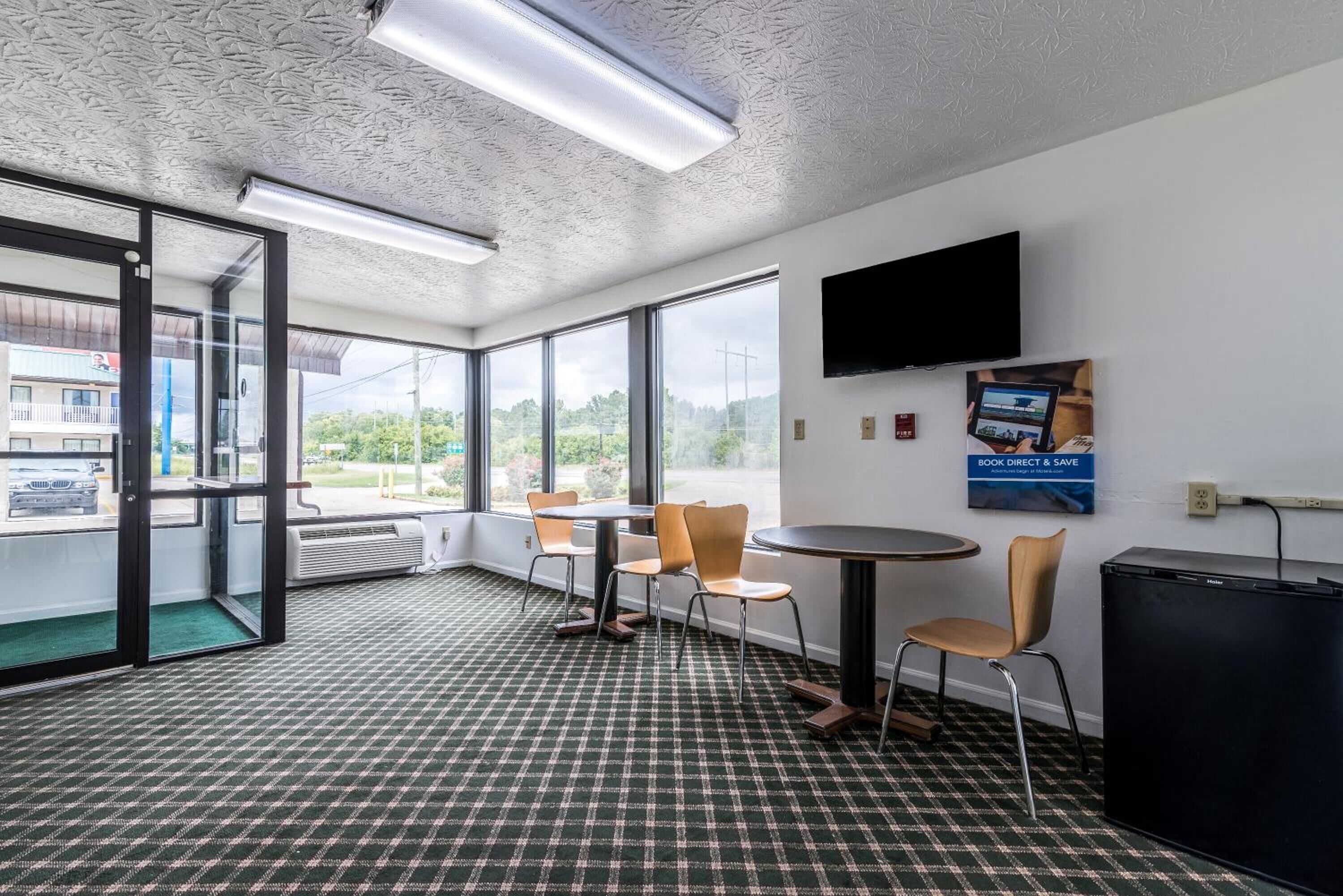 Un espacio de oficina moderno con alfombra a cuadros, un televisor de pantalla plana montado en la pared y un letrero que dice 'Book Direct & Save'.