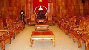 Une pièce avec un fauteuil rouge placé au centre, un emblème en forme d’étoile et des rangées de chaises en bois.