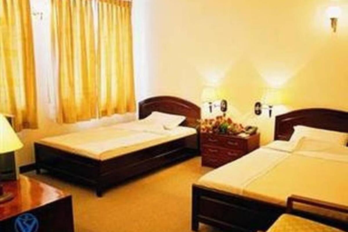 A hotel room with two beds, a nightstand, a lamp, and a dresser.