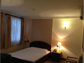 Hotellihuone, jossa on yksi sänky, yöpöytä lampun kanssa ja tuoli.