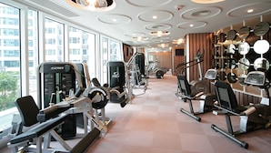 A gym with various exercise equipment, large windows, and a modern ceiling design. - Kowloon Harbourfront Hotel (Kowloon)