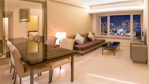 A modern living room with a glass dining table, a sofa with cushions, a coffee table, and a view of a cityscape at night. - Kowloon Harbourfront Hotel (Kowloon)