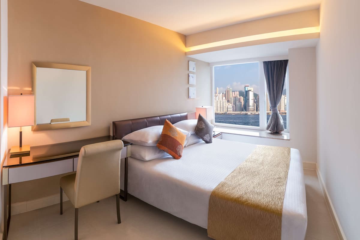 A hotel room with a bed, desk, chair, and a large window with a city view.