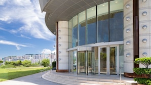 A modern building with a curved facade, large glass windows, and a well-maintained lawn area. - Kowloon Harbourfront Hotel (Kowloon)