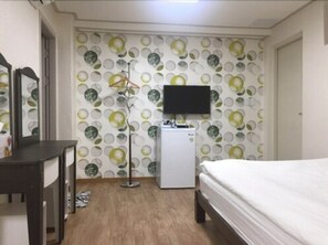 A bedroom with a bed, a desk, a TV, and a refrigerator.