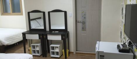 A hotel room with two beds, a desk with a mirror, a small refrigerator, and a door with a floral design.