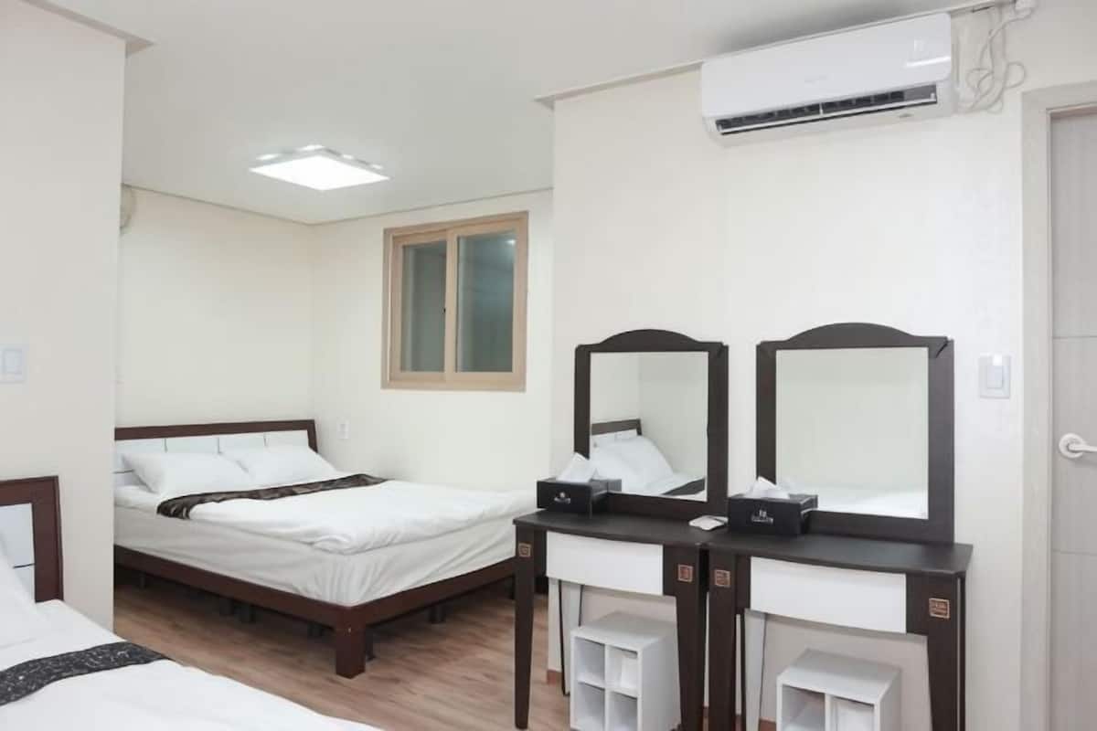 A hotel room with two beds, a desk with a mirror, a small cabinet, and an air conditioning unit.