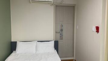 Quarto com cama, ar condicionado, porta com desenho floral e luz de emergência vermelha.