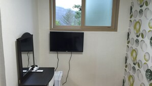Um quarto com televisão fixada na parede, uma escrivaninha com computador e impressora, e um radiador.