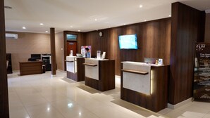 A reception area with three wooden reception desks, a television mounted on the wall, and a signboard with text. - Sanghyang Indah Spa Resort (Anyer)