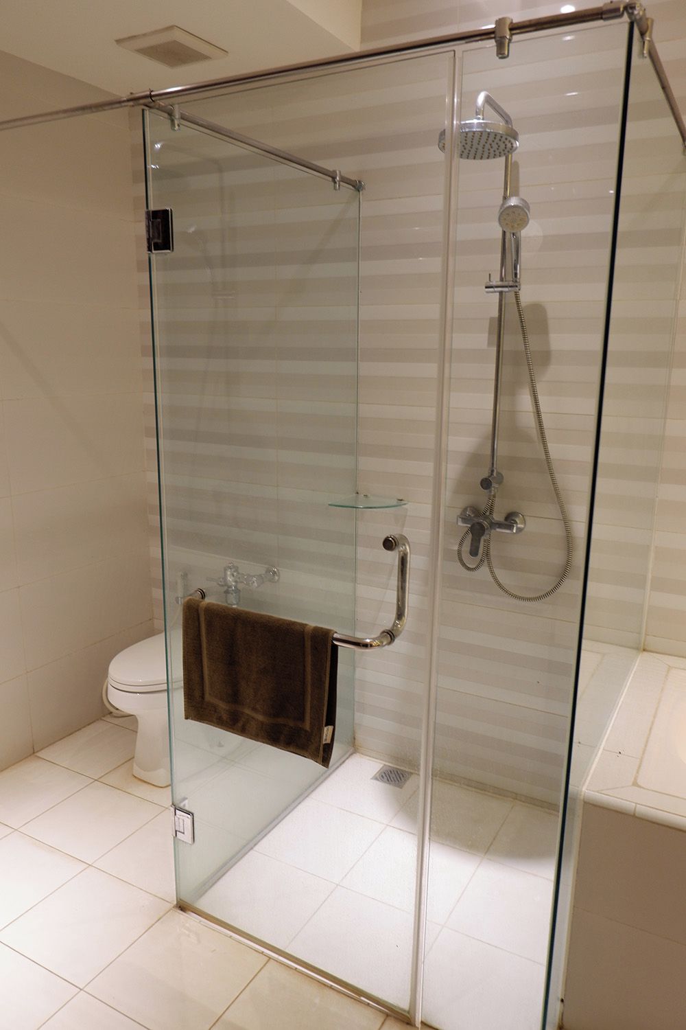 A glass-enclosed shower stall with a handheld showerhead and a wall-mounted faucet.