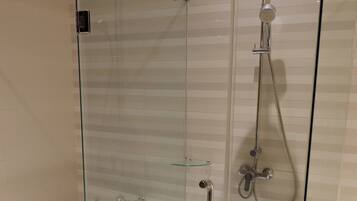 A glass-enclosed shower stall with a handheld showerhead and a wall-mounted faucet.