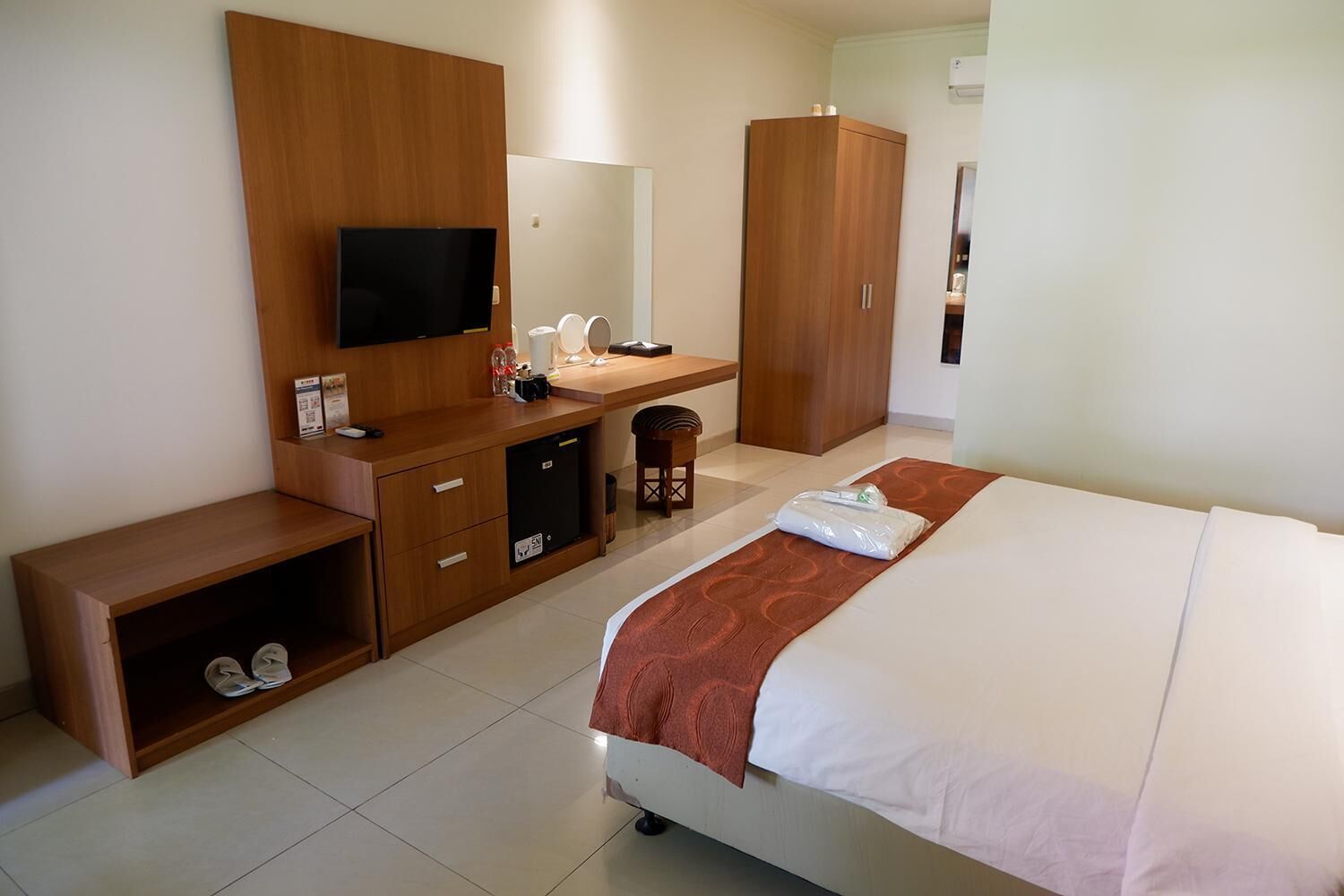 Habitación de hotel con cama, televisor, escritorio con computadora, armario y zapatero.