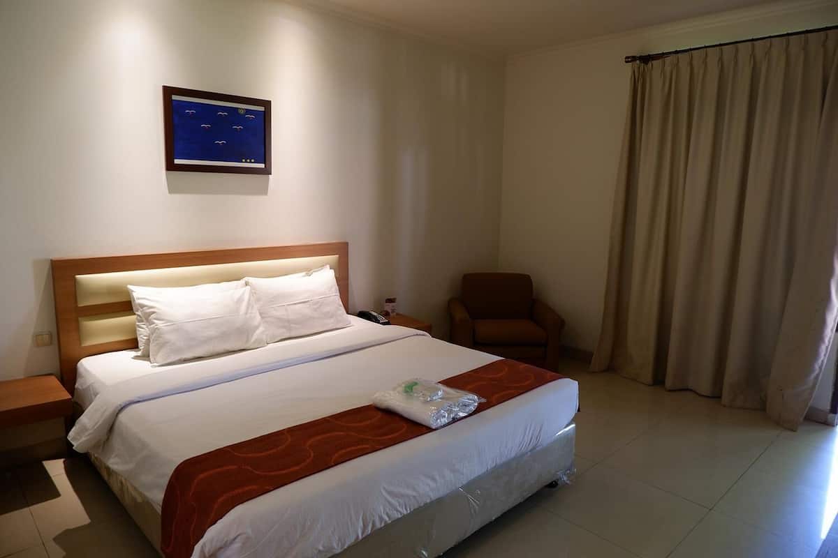 Una habitación de hotel con una cama, una silla, una mesita de noche, un teléfono y un cuadro en la pared.