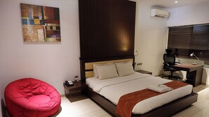 A modern bedroom with a large bed, a red bean bag chair, a desk with a computer, and a window with blinds. - Sanghyang Indah Spa Resort (Anyer)
