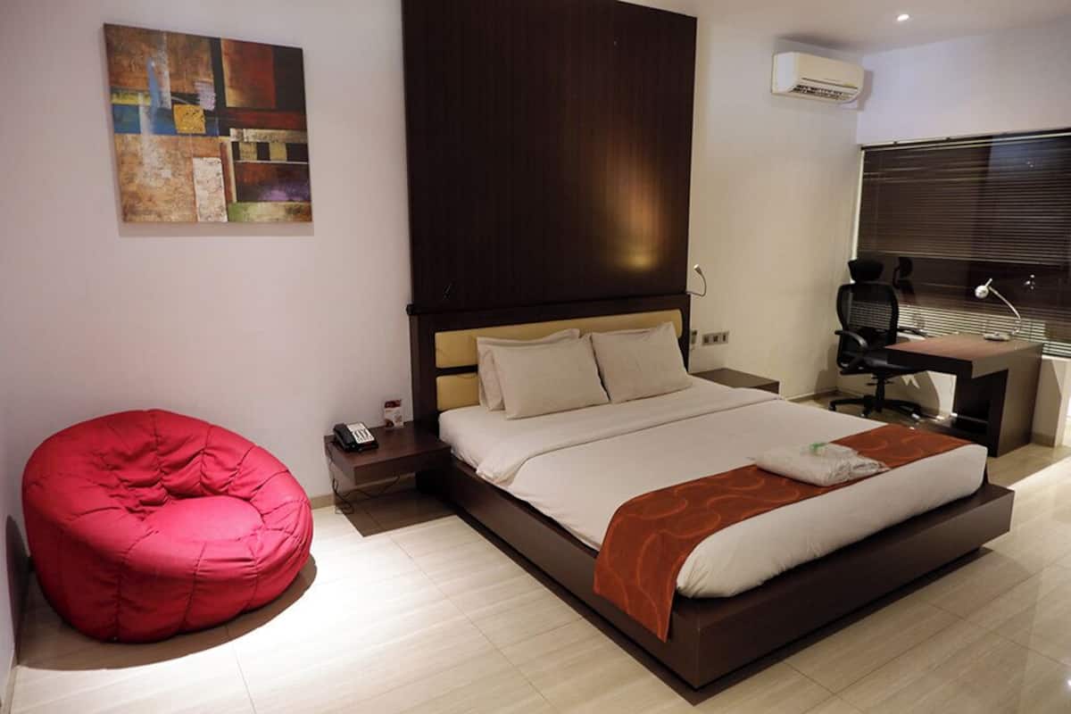 Un dormitorio moderno con una cama grande, un sillón de peluche rojo, un escritorio con una computadora y una ventana con persianas.