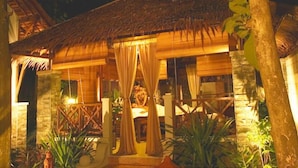 A thatched-roof structure with a bed and curtains, surrounded by plants and stone walls. - Sanghyang Indah Spa Resort (Anyer)