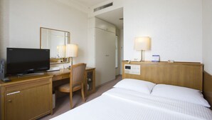 A hotel room with a bed, a desk with a television, a chair, and two bedside lamps.