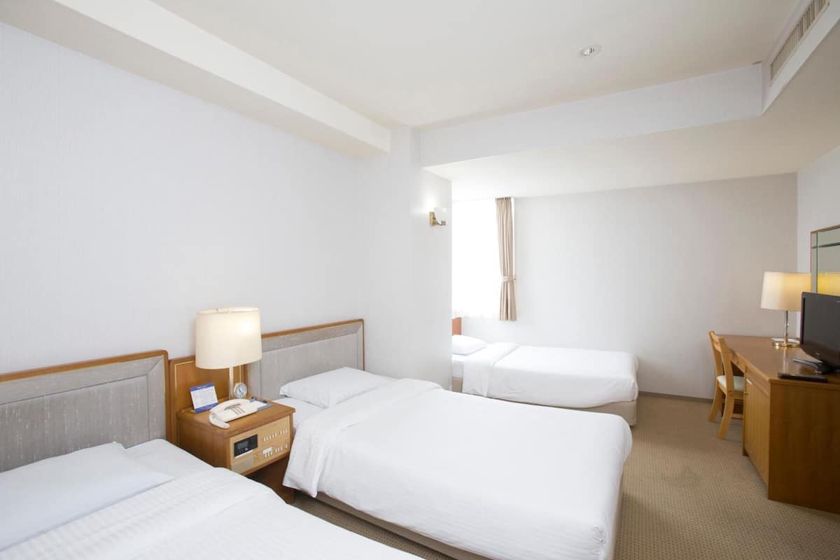 Une chambre d’hôtel avec deux lits simples, un bureau avec une chaise, une télévision et une table de chevet avec une lampe et un téléphone.