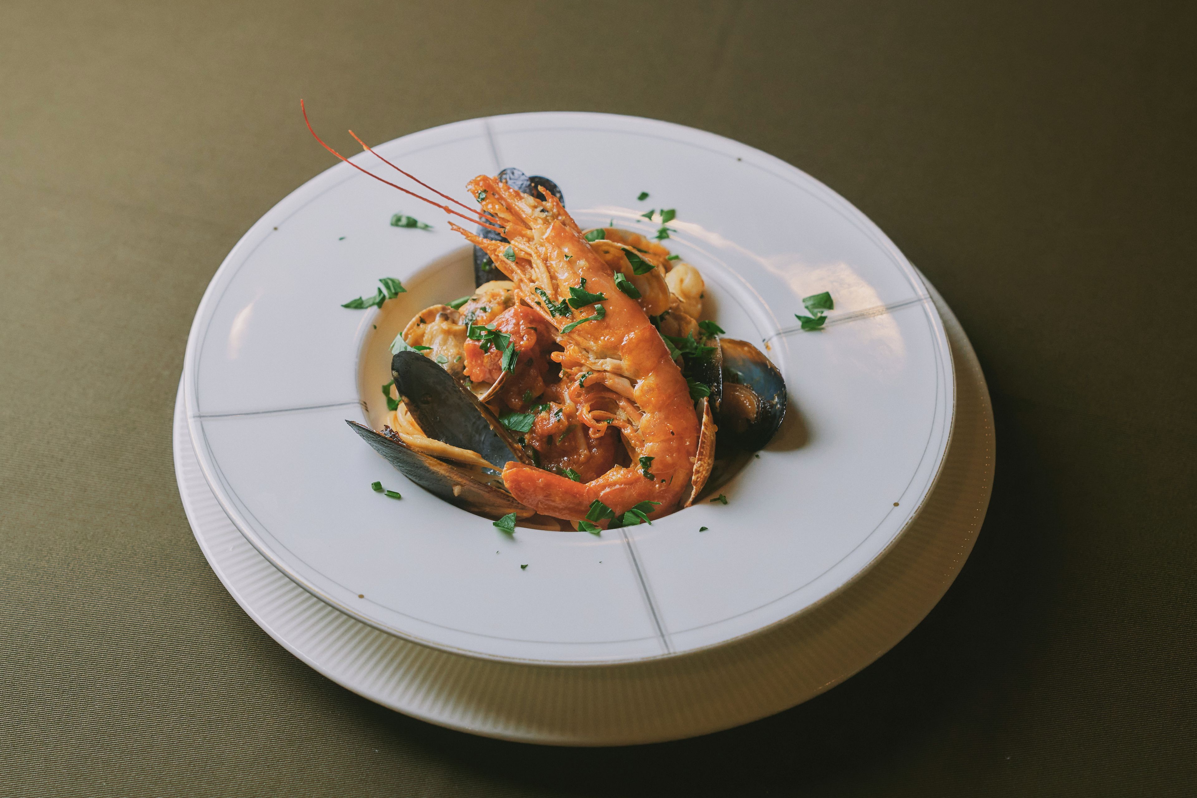 En tallerken med fisk og skaldyr, herunder rejer og muslinger, pyntet med krydderurter.