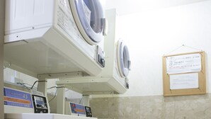 A laundry room with two washing machines and a dryer, a bulletin board with a notice, and tiled walls.