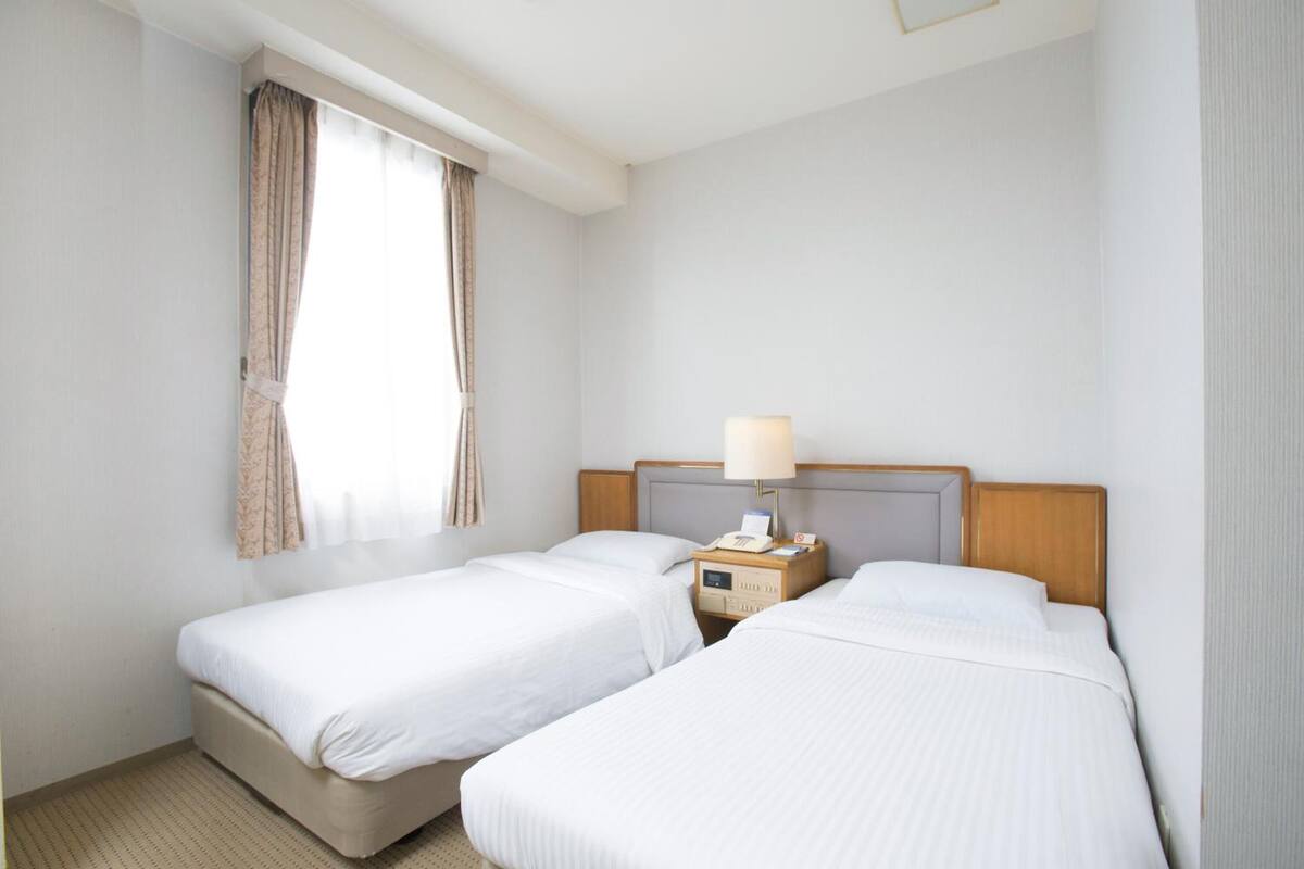 Une chambre d’hôtel avec deux lits, une table de chevet avec une lampe et une fenêtre avec des rideaux.