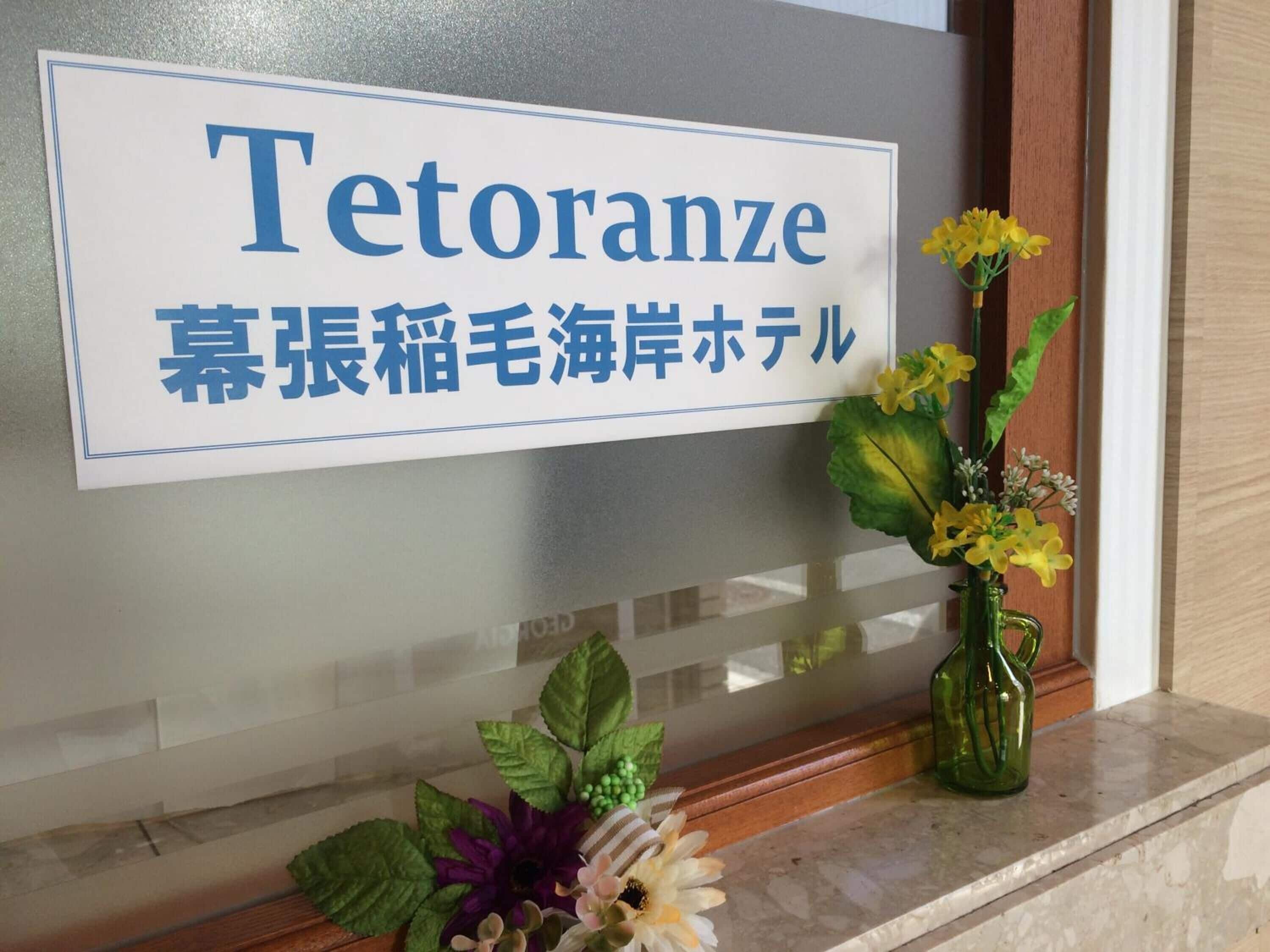 Un comptoir d’accueil avec une enseigne indiquant « Tetoranze » et un texte en japonais en dessous. Un vase rempli de fleurs jaunes est posé sur le comptoir.