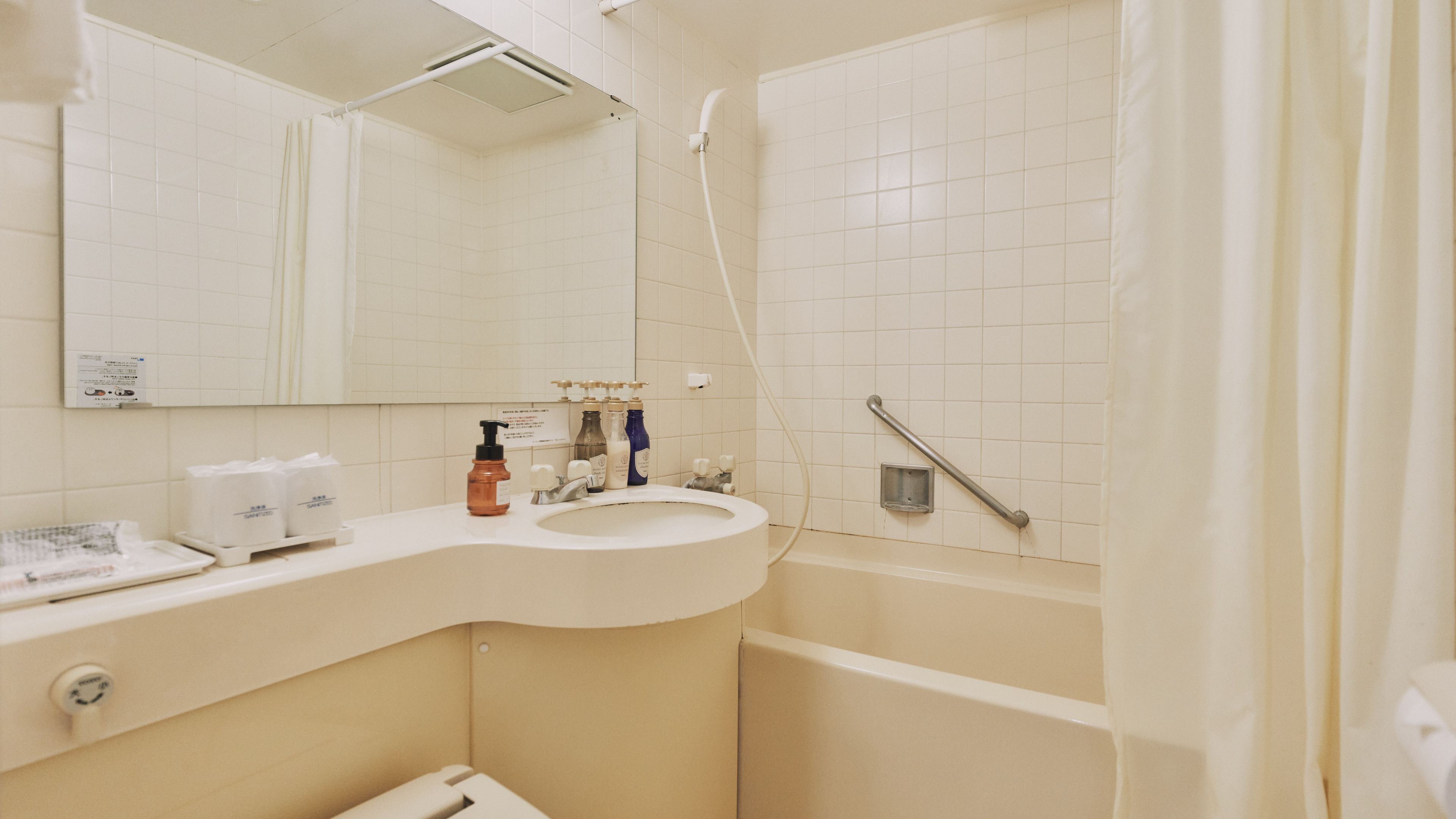 A bathroom with a white sink, mirror, and a shower area with a grab bar.