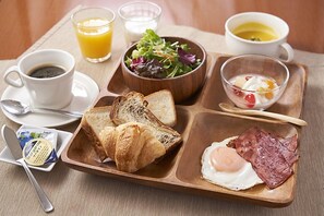 A breakfast tray with toast, croissants, ham, and an egg, along with a bowl of salad, a glass of orange juice, a cup of coffee, and a bowl of yogurt. - Tetoranze Makuhari Inagekaigan Hotel (Chiba)