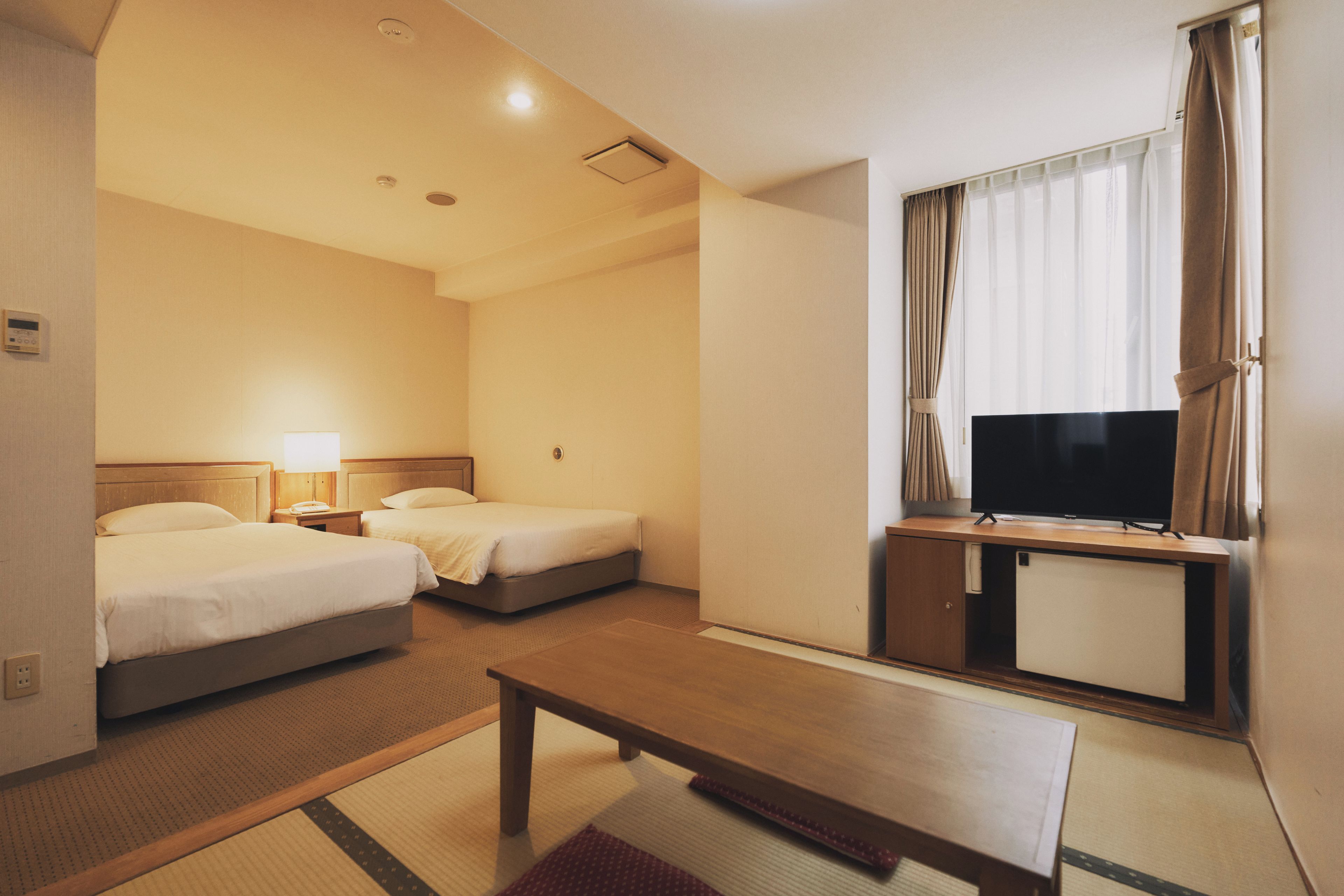 A hotel room with two beds, a TV, a desk, and a window with curtains.