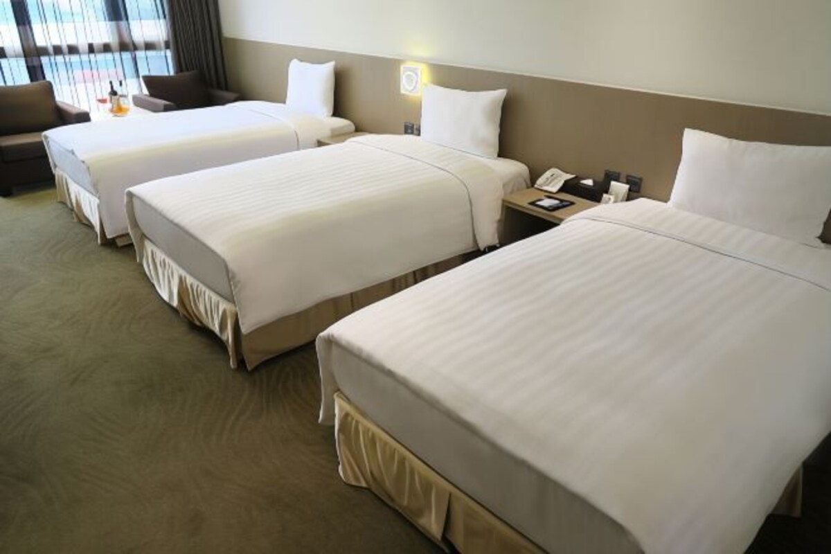 Una habitación de hotel con tres camas individuales, un sofá y una mesita de noche con lámpara.