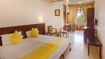 A hotel room with a bed, a desk, chairs, a television, and a balcony with curtains.