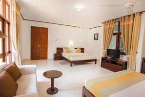 Una habitación de hotel con cama, televisor, sofá, una mesita y un ventilador de techo.