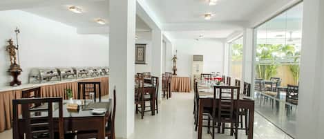 Un comedor amplio con varias mesas y sillas, un ventanal con vistas a la vegetación y una estatua en la pared.