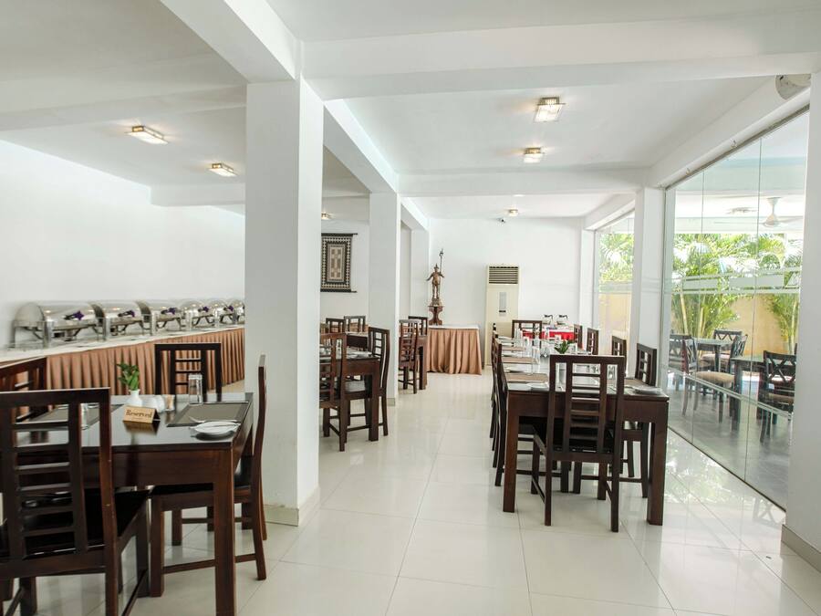 A spacious dining area with multiple tables and chairs, a large window with a view of greenery, and a statue on the wall.