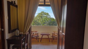 A room with a wooden desk, a chair, and a table with two chairs outside, through a window with curtains. - Lavendish Okrin Hotel (Kataragama)
