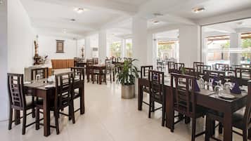 A spacious dining area with multiple tables and chairs, large windows allowing natural light, and a central potted plant.