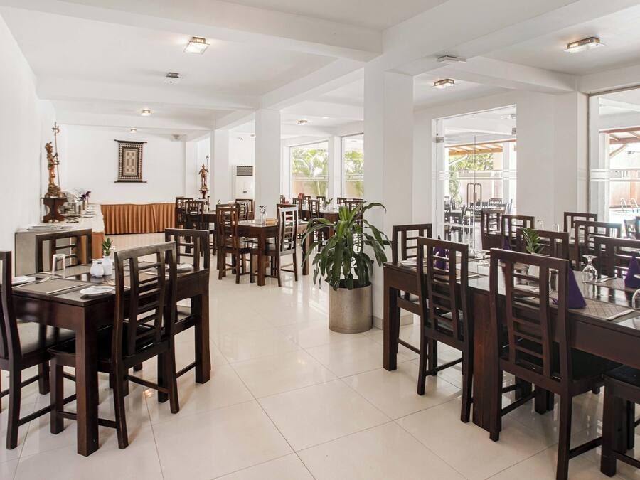 A spacious dining area with multiple tables and chairs, large windows allowing natural light, and a central potted plant.
