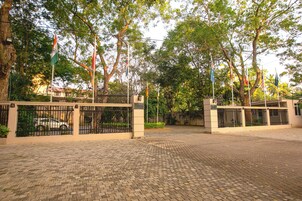 Un acceso pavimentado con una puerta metálica, rodeado de árboles y varias banderas.