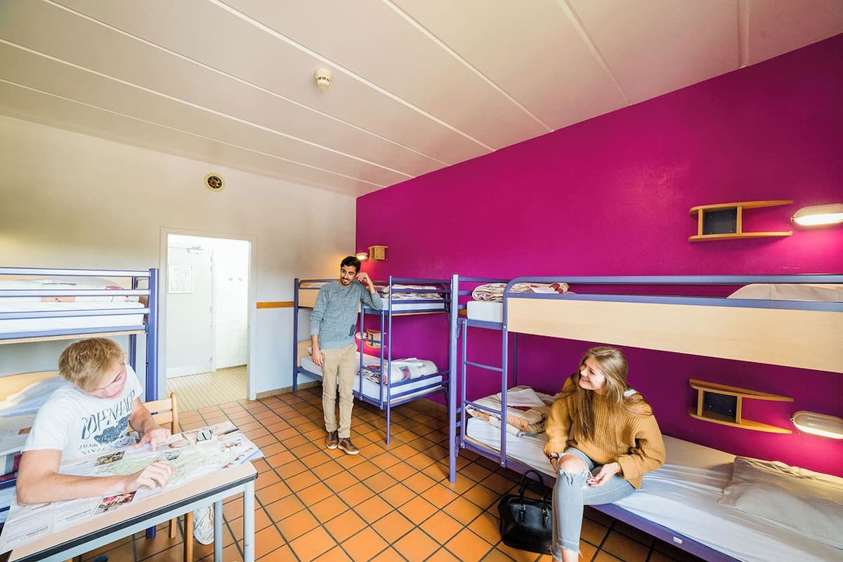 A dormitory room with bunk beds, a table with newspapers, and a door.